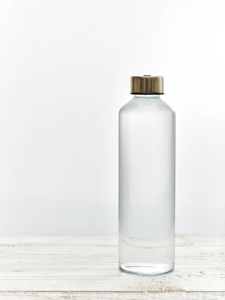 Garrafa de água potável de vidro reutilizável na mesa de madeira branca
 - Foto, Imagem