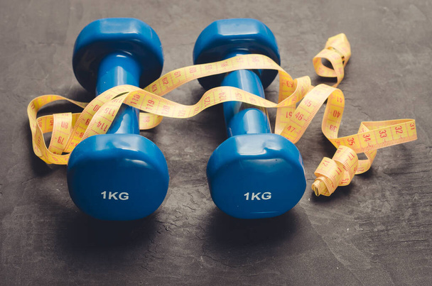 Dumbbells and measuring tape/fitness concept with blue dumbbells and measuring tape on a dark background - Photo, image