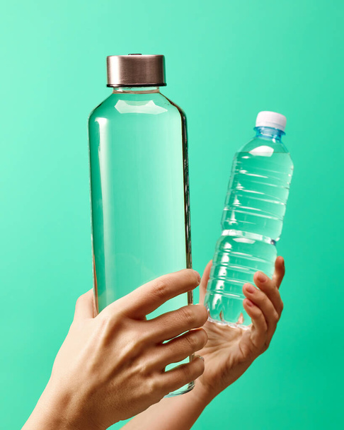 Μηδέν έννοια αποβλήτων - επαναχρησιμοποιήσιμη γυάλινη φιάλη νερού vs μίας χρήσης πλαστικό μπουκάλι σε πράσινο φόντο μέντα - Φωτογραφία, εικόνα