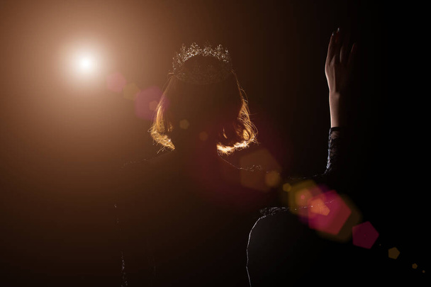 Portrait Silhouette Shadow Back Rim Light of Miss Pageant Beauty Queen Contest Silver Diamond Crown wave hand express feeling smile, studio lighting dark black background, turn back head to camera - Photo, Image