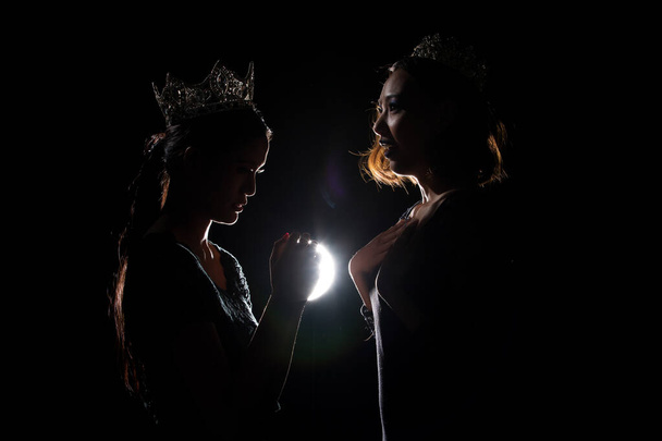 Two Silhouette Shadow Back Rim Light of Miss Pageant Beauty Queen Contest with Silver Diamond Crown glad to get final moment announce Winner prize, hand to face, studio lighting dark black background - Photo, Image