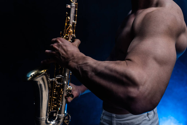 Muscular man with naked torso playing on saxophone with smoked colorful background  - Photo, Image