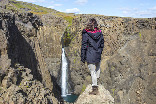 A young woman looking at Hengifoss, the third tallest waterfall in Iceland - Fotografie, Obrázek