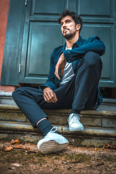 Street Style, a young Caucasian model sitting by a blue door - Φωτογραφία, εικόνα