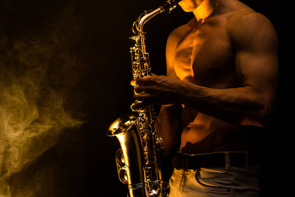 Muscular man with naked torso playing on saxophone with smoked colorful background  - Foto, Imagem
