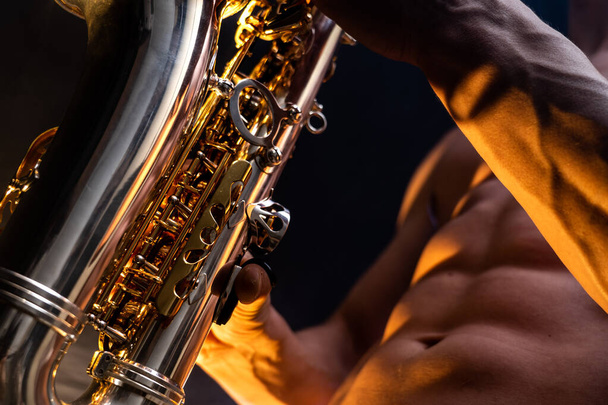 Hombre musculoso con torso desnudo tocando en saxofón con fondo colorido ahumado
  - Foto, Imagen