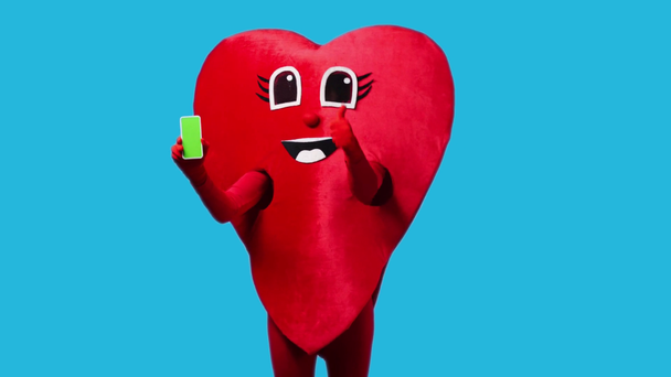 osoba w czerwonym sercu kostium gospodarstwa smartfon izolowany na niebiesko - Materiał filmowy, wideo