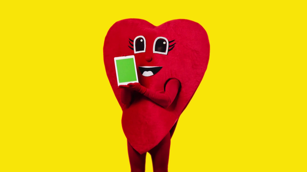person in red heart costume holding digital tablet isolated on yellow - Footage, Video