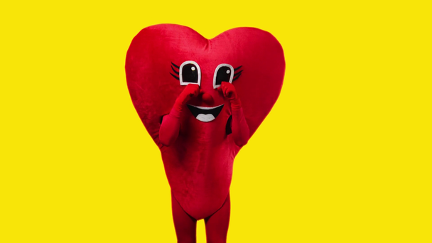 person in heart costume touching cartoon eyes isolated on yellow - Footage, Video