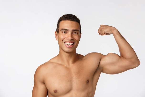 African American teenager shows muscles on arm. Isolated on white background. Studio portrait. Transitional age concept. - 写真・画像