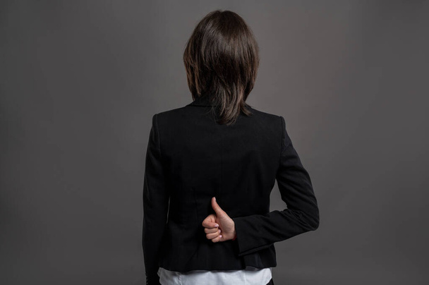 Retrato de una maravillosa joven mujer de negocios con traje negro y camisa mostrando pulgares hacia arriba mano en la espalda posando sobre un fondo gris aislado
 - Foto, Imagen