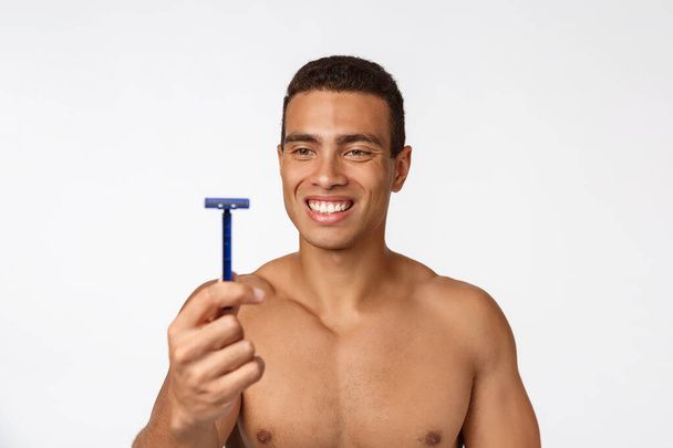 Close up of a happy naked african man holding razor isolated over gray background. - Photo, Image