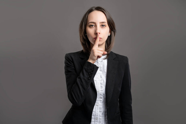 Portrait of wonderful young business woman wering black suit and shirt showing shh gesture poseing on isolated gray background - Photo, image
