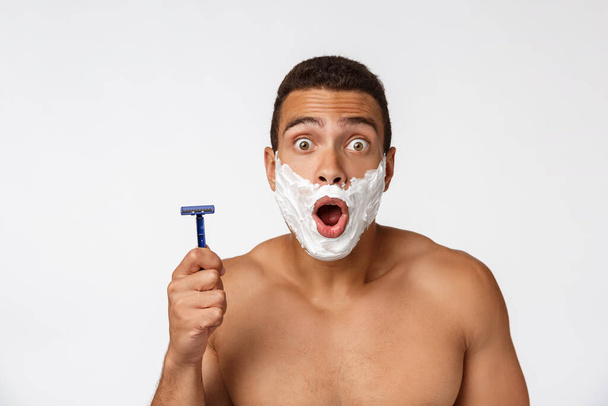 Закрыть счастливый голый африканский мужчина с лицом в пены для бритья держа бритву изолированы на сером фоне
. - Фото, изображение