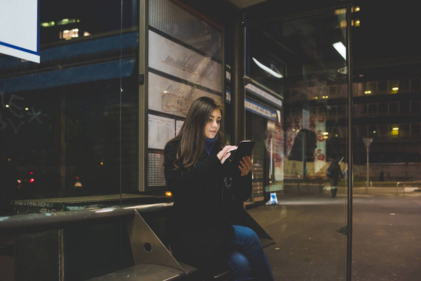 若い女性がスマートフォンを使ってバス停に座っています-技術、パブ、通勤コンセプト - 写真・画像