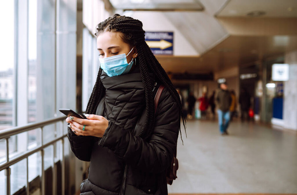 Girl in protective sterile medical mask on her face with a phone in  quarantine city. Woman using the phone to search for news. The concept of preventing the spread of the epidemic.  - Photo, Image