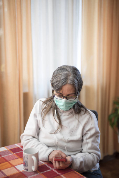Vírus Corona. Mulher doente do vírus corona com smartphone, vestindo proteção respiratória de segurança e recuperação da doença em casa. Paciente isolado para prevenir infecção
 - Foto, Imagem