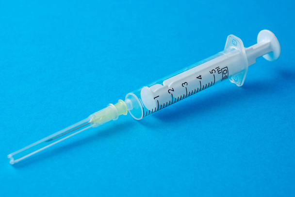 Detailní záběr průhledné plastové injekční stříkačky s krytou jehlou na modrém pozadí vodorovně s kopírovacím prostorem - Fotografie, Obrázek