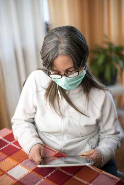 Corona-virus. Sairas nainen koronavirus tabletilla, yllään turvallisuus hengitys suojelua ja toipuminen sairaudesta kotona. Potilas eristetty infektion ehkäisemiseksi
 - Valokuva, kuva