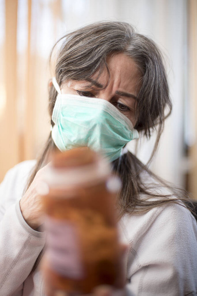 Ιός Κορόνα. Άρρωστη γυναίκα από τον ιό του στέμματος φορώντας προστατευτικό αναπνοής ασφαλείας, με ένα δοχείο με φάρμακα και ανάρρωση από την ασθένεια στο σπίτι. Ασθενής απομονωμένος για πρόληψη λοίμωξης - Φωτογραφία, εικόνα