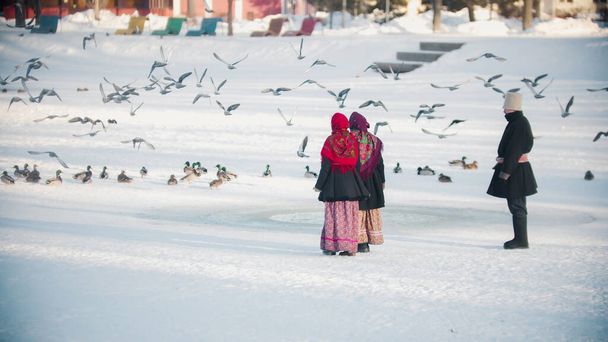 ロシアの伝統-美しい服の人々は凍った池でハトを追いかけています - 写真・画像