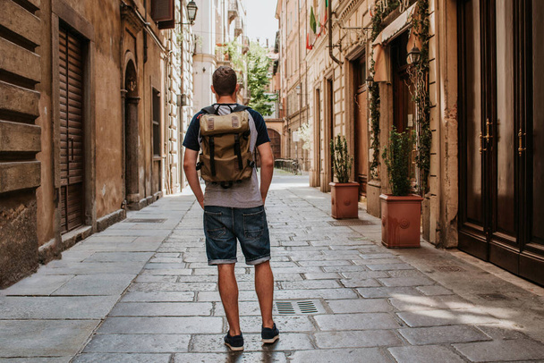 A man with a backpack walks through the streets of the city. Tourist enjoy holidays in Europe. Beautiful old historical architecture. Italian weekend. Travel to Turin, Italy. Adventure lifestyle - Zdjęcie, obraz