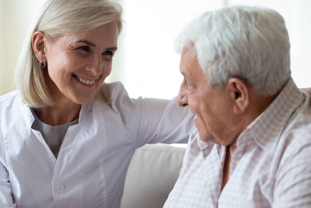 Gülümseyen orta yaşlı kadın doktor yaşlı erkek hastayla konuşuyor. - Fotoğraf, Görsel