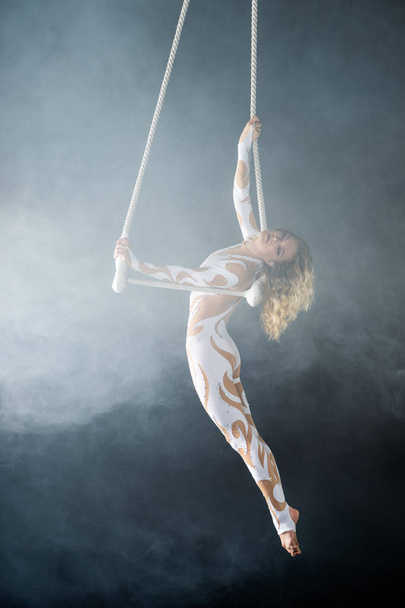 A young girl performs the acrobatic elements in the air trapeze. Studio shooting performances on a black background - Photo, Image