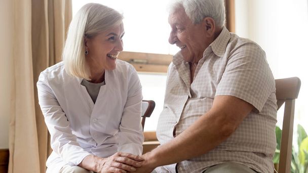 Friendly smiling mature doctor holding happy older patient hands - Photo, Image