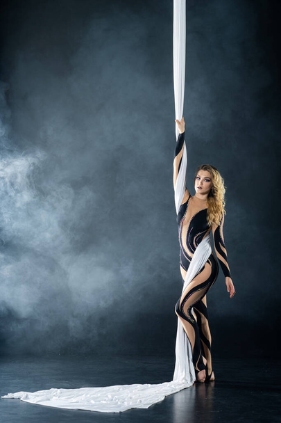 A young girl performs the acrobatic elements in the airrial silk. Studio shooting performances on a black background - Valokuva, kuva
