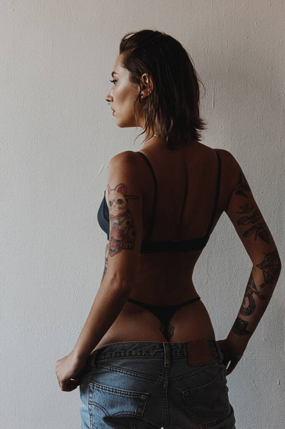 Sexy woman with tattoos wearing lingerie and jeans - Photo, image
