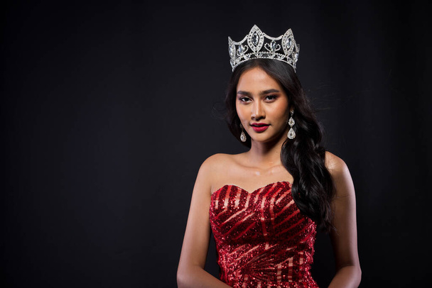 Portrait of Miss Pageant Contest in Asian woman Red Evening Ball Gown with Diamond Crown Sash, fashion make up face eyes love hair style, studio light dark background isoled copy space - Фото, зображення