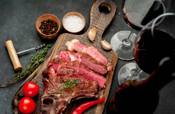 Bone-In ribeye herb grilled steak slices with red wine glasses on rustic table background - Foto, imagen