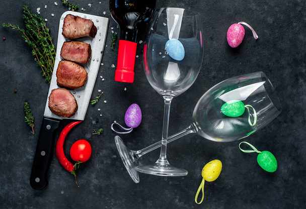 uova colorate con fette di carne e bottiglia di vino rosso con bicchieri su sfondo rustico
 - Foto, immagini