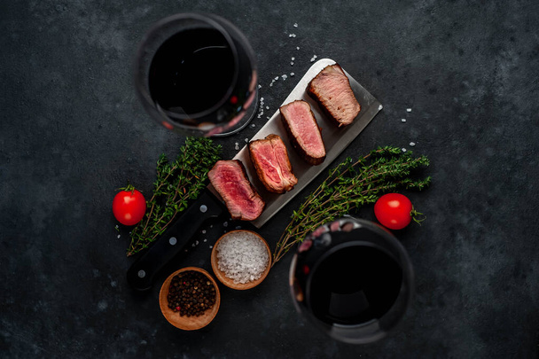 grilled medium rare medallion steak slices with herbs and wine glasses on gray rustic table background - Valokuva, kuva