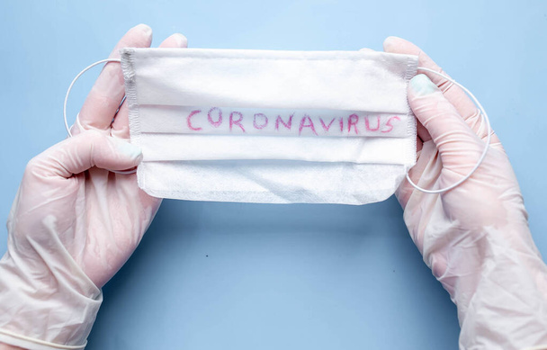 person hands in medical gloves holding mask with words coronavirus isolated on blue background - Photo, Image
