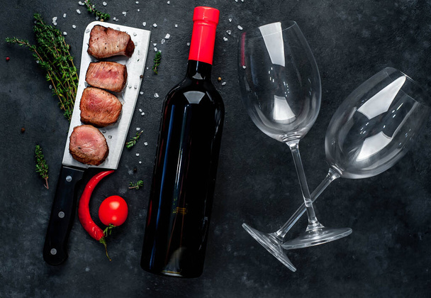 grilled meat slices and red wine bottle with glasses on rustic background - Photo, Image