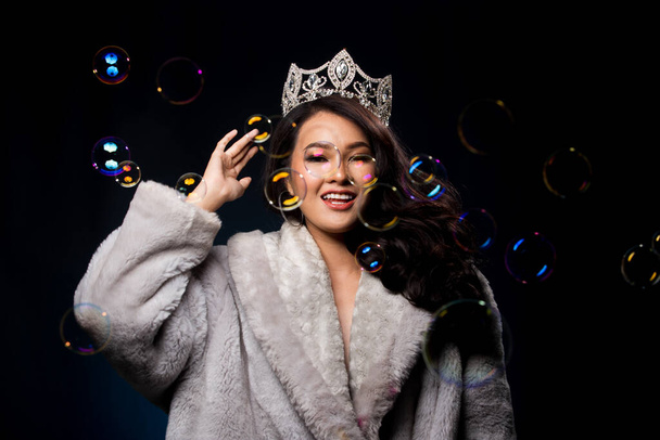 Portrait Miss Pageant beauty Contest in Asian Fur Gray winter jacket dress with Silver Diamond Crown Sash, fashion make up face hair style, studio lighting dark background bubble - Фото, изображение