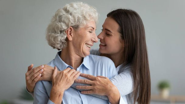 Smiling adult daughter and senior mother hug at home - Photo, Image
