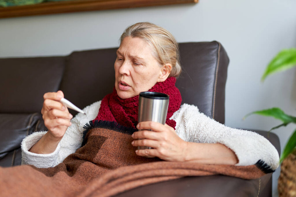 Woman is having flu and she is using thermometer. Sick with a rhinitis woman dripping nose. - Photo, image