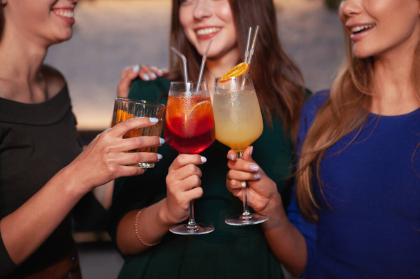 Cropped shot of happy female friends clinking cocktail glasses together, celebrating together - 写真・画像