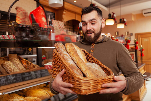Junger Mann wählt beim Bäcker frisches Brot aus dem Korb. Glücklicher Mann kauft Brot im Backhaus - Foto, Bild