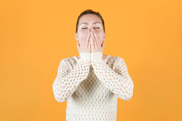 young girl yawns covering her mouth. Isolated on orange-yellow background - Фото, зображення