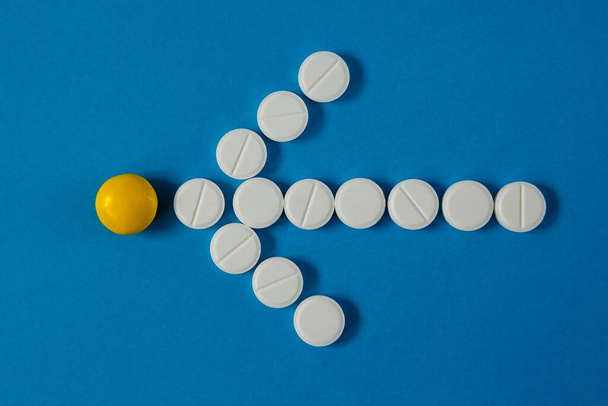 arrow of white pills indicates a yellow pill, on a blue background from above - Фото, изображение