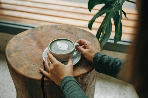 Girl drinks aromatic fresh and healthy green matcha latte tea in a cafe. - Фото, зображення