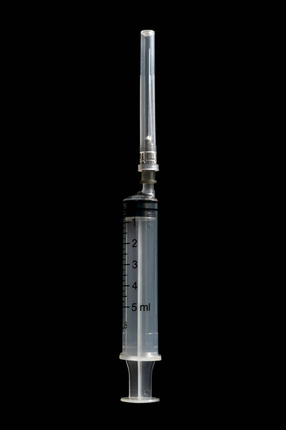 Медицинский шприц с защитной крышкой изолирован на черном фоне. Инъекционный инструмент
 - Фото, изображение