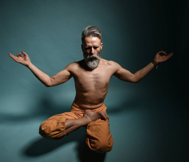 Old man with grey beard doing yoga, pilates, fitness training, stretching exercise, asana levitates or balance workout on floor - Foto, Bild