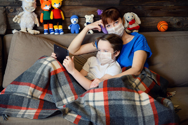 Photo in the home interior mom cares for a boy of 9 years old, sitting next to quarantine on the couch - 写真・画像