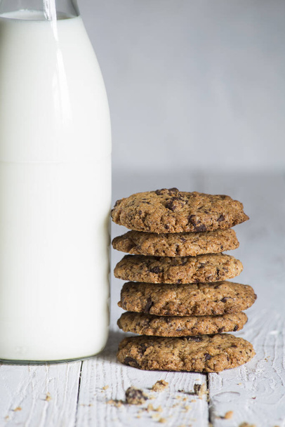 A chocolate cookies stacked next to a milk bottle on top of a white wooden board, with space for text - Foto, Bild