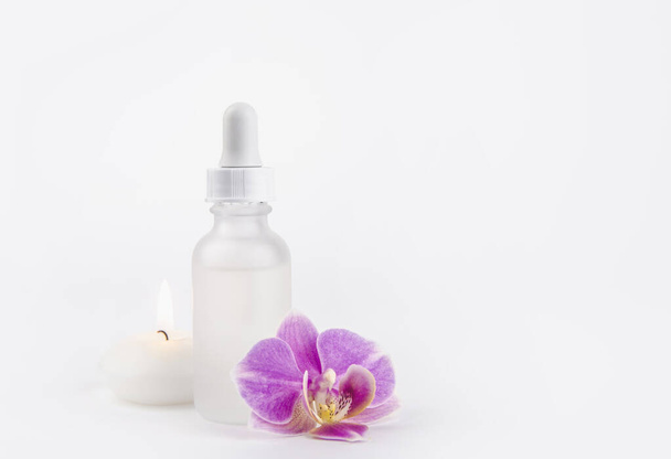 Blanco luxe witte matte cosmetische druppelflesje met leeg etiket voor cosmetische medische producten en achtergrondconcept. Studio shot, met roze glamoureuze orchidee bloesem en kaars branden. - Foto, afbeelding